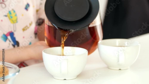 Two little girls pours fruit tea into cups with baking homemade cookies
