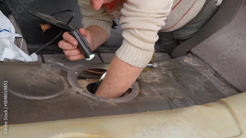 Professional auto mechanic installing a new electric fuel pump module into the gas tank of a modern car during a vehicle repair service at the garage, ensuring proper fuel system function