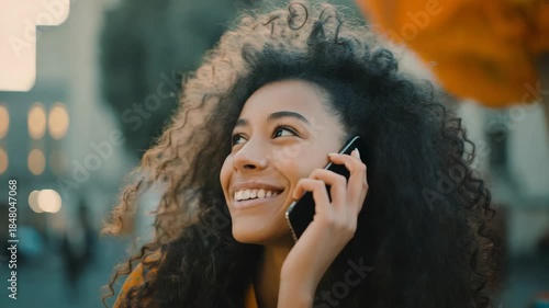 Happy woman with curly hair smiles while talking on her smartphone