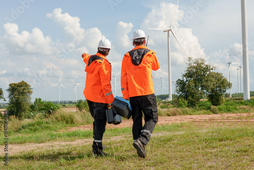 Engineer team walking toward wind turbine carrying maintenance toolboxes pointing toward renewable energy task promoting sustainable electric generation teamwork innovation outdoor green technology