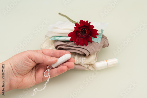Foto Hand holding a tampon beside folded lingerie, pads, and a red flower, symbolizing menstruation, feminine care, body awareness, and a calm, respectful view of women’s health