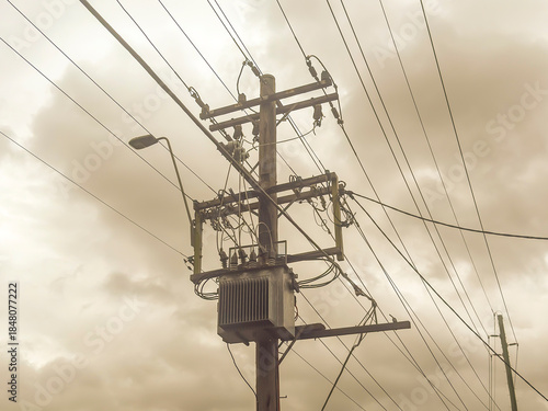 Photograph of a pole mounted electricity step down transformer on a street in a residential precinct on a cloudy and stormy day in regional Australia.