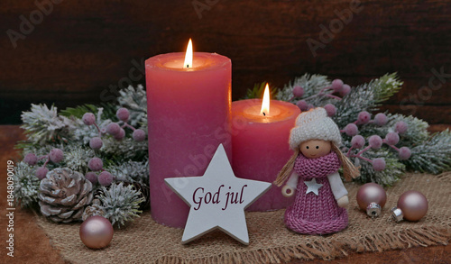 Christmas card: Pink candles with Christmas decorations and a small doll on a star bears the Swedish greeting God jul.