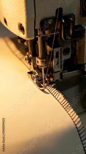 Close-up shot of a white serger sewing machine needle rapidly stitching an overlock seam onto light fabric under warm light