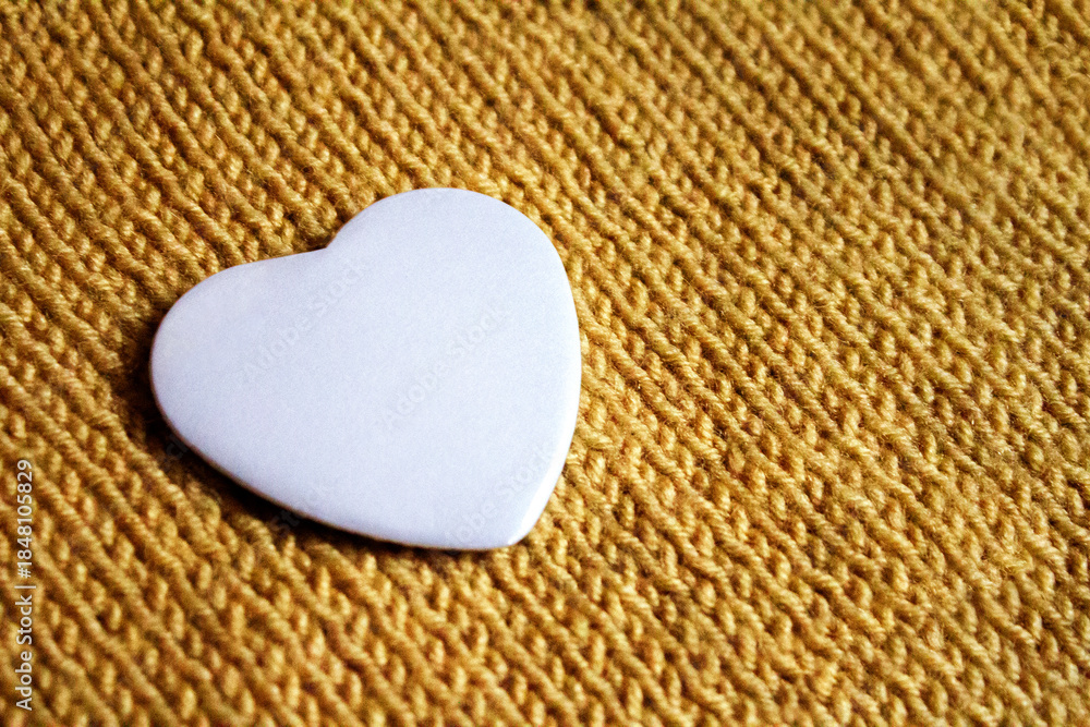 Obraz premium Heart Badge Mockup. White heart badge on textured knitted fabric, ideal for romantic or custom designs. A blank heart-shaped pin resting on warm textile, perfect for personal artwork display