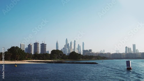 Yacht sail pov with amazing view of Dubai Marina modern skyline featuring tall skyscrapers, waterfront, and lush greenery of Eco Park island with palm trees