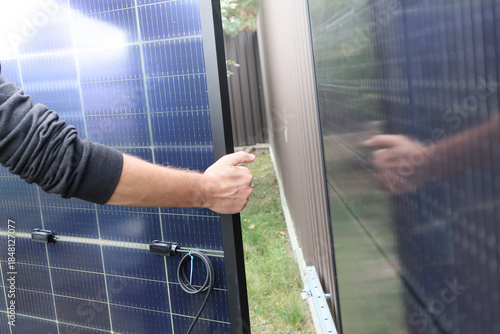 Worker's hand holding a solar panel during installation on a metal fence.