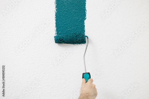 Hand holding paint roller applying teal paint on textured wall, showcasing home improvement and creative interior design concepts. free space