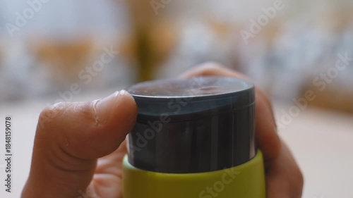 A man's hand opens the plastic lid of a reusable thermos bottle of water, shampoo or cream . A daily facility for hydration, sports, travel and the promotion of a sustainable, eco-friendly lifestyle