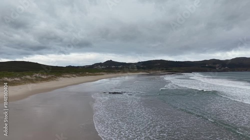 Ocean waves breaking on a sandy beach below a cloudy sky in ferrol, galicia