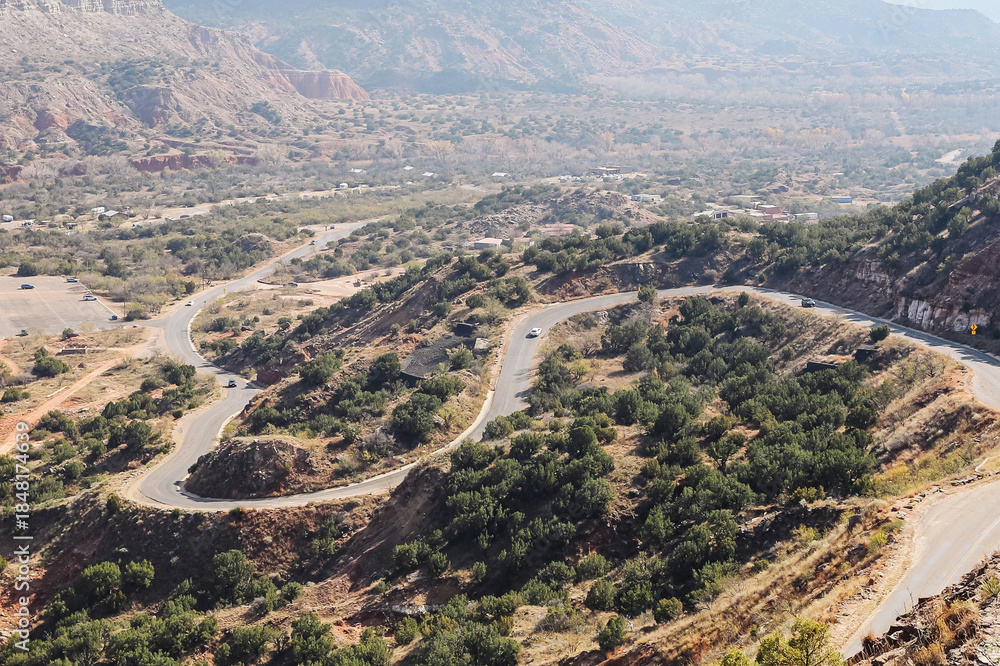Fototapeta premium Winding mountain road landscape. Scenic serpentine highway view. Curved asphalt road through hills. Natural valley panorama from above. Remote countryside travel route. Rugged terrain and greenery