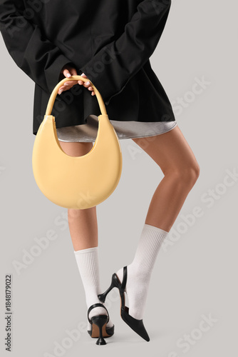 Beautiful young woman with yellow leather bag on grey background © Pixel-Shot