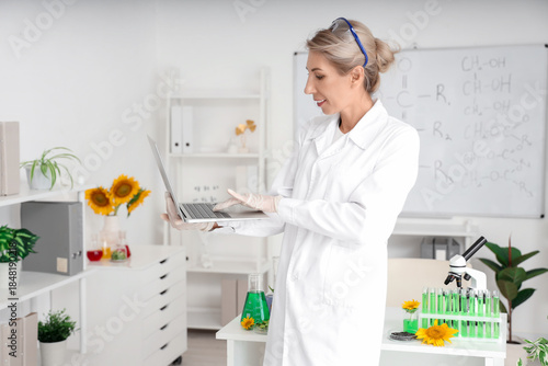 Happy female scientist with flasks of sunflower samples and working in labora...