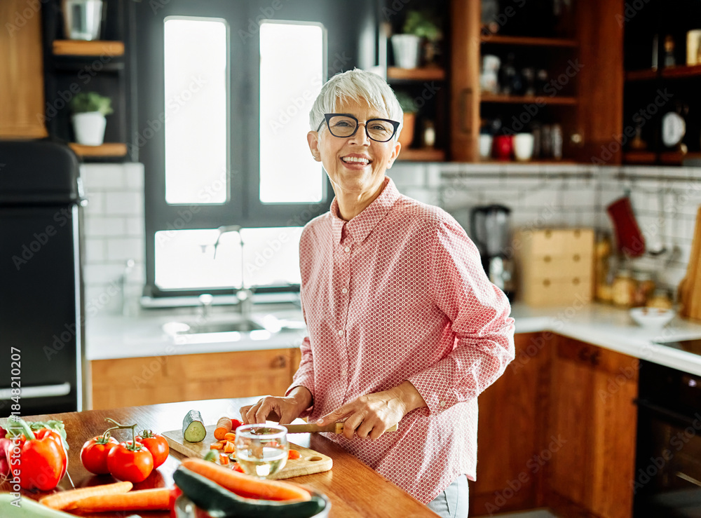 Fototapeta premium Portrait of happy senior mid aged mature woman prepering meal with fresh vegatebles in kitchen at home