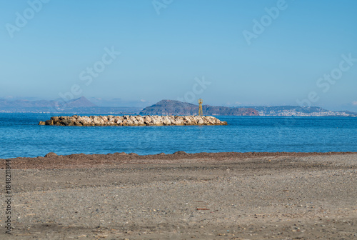Calm sea with rocky breakwater and navigation beacon under clear sky
