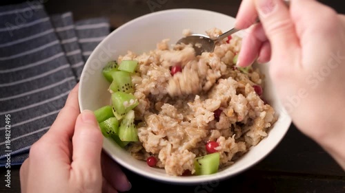Breakfast oatmeal porridge with kiwi and cranberries. Female hands eating oatmeal for breakfast. POV view