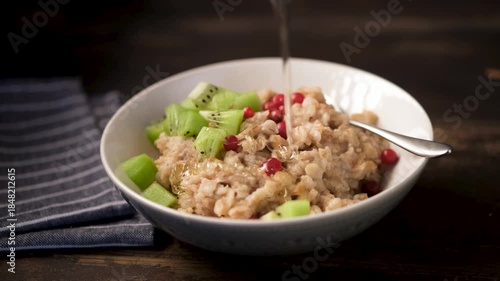 Breakfast boiled oatmeal porridge with fruits, berries and honey. Liquid honey pouring on oatmeal porridge bowl