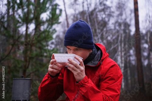 A young man eating instant noodles in nature. Lunch during a hike in the forest, fast food at a picnic