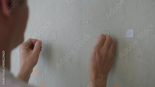 Rear view of contractor pressing double-sided adhesive tape onto weathered wallpaper, preparing for home renovation and decorating project, close-up detail of diy repair work, close-up, slow motion.