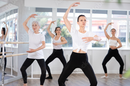 Group of slender women of different ages are learning various dance and ballet movements in the studio