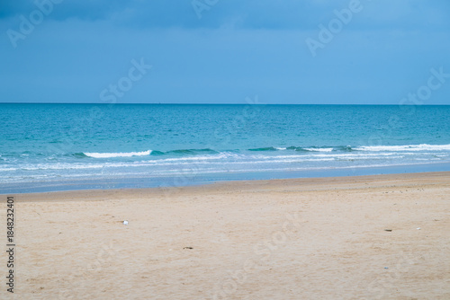 Wide sandy beach with calm sea and blue sky, coastal city on the horizon creating a peaceful seaside landscape with copy space.
