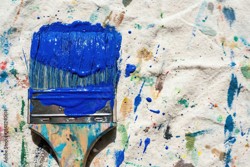Blue Brushstrokes: A close-up view unveils a paint-laden brush, its bristles saturated with vibrant blue hue, set against a backdrop of splattered colors, revealing the artistic process.