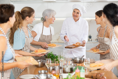 Tableau sur toile Young female chef at master class teaches group of people how to cook chicken
