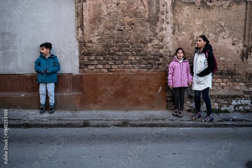 Mother and children waiting on urban street by brick wall