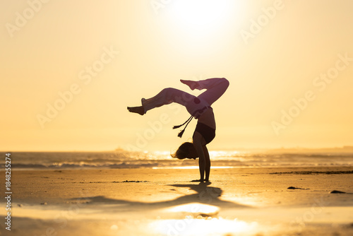 Capoeira practitioner performing acrobatics on beach at sunset