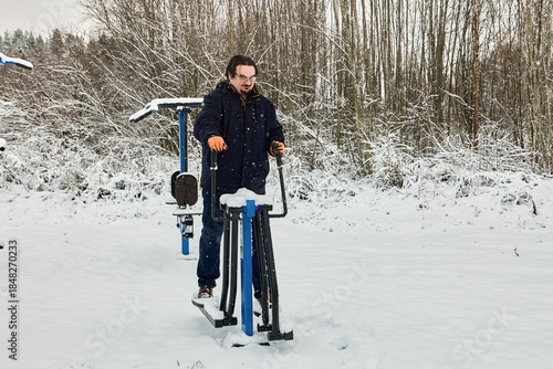 Mature man exercises on outdoor fitness equipment on snowy day.