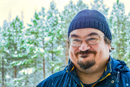 Heavily dressed stocky man trying to hold smile in winter forest closeup