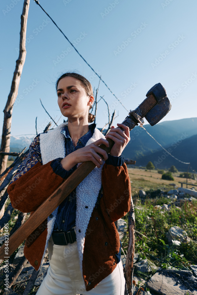 Fototapeta premium Woman with shovel on countryside farm near mountains, outdoor farming scene with agricultural tool and rural gardener in jacket preparing soil for planting or vineyard maintenance.