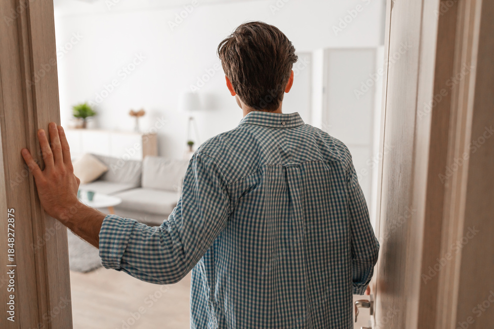 Naklejka premium A young man stands in the doorway of his new apartment, casually dressed. He gazes at the modern interior design as he prepares to step inside and explore the space.