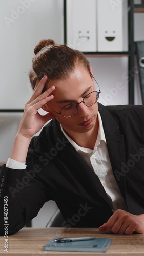 Tired exhausted stressed young businessman looking at large pile of books and looking at volume of work with sad face while preparing for exams at home office. Overwork education business concept.