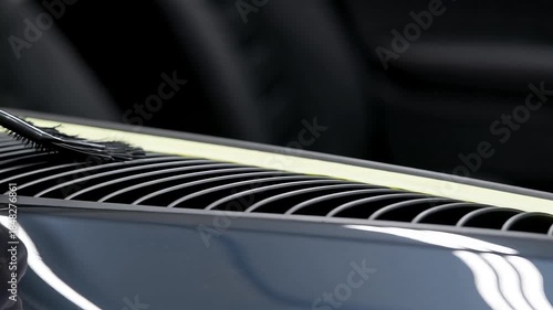 Person hand cleaning plastic car air vent with small brush on dark dashboard background representing professional detailing and vehicle maintenance