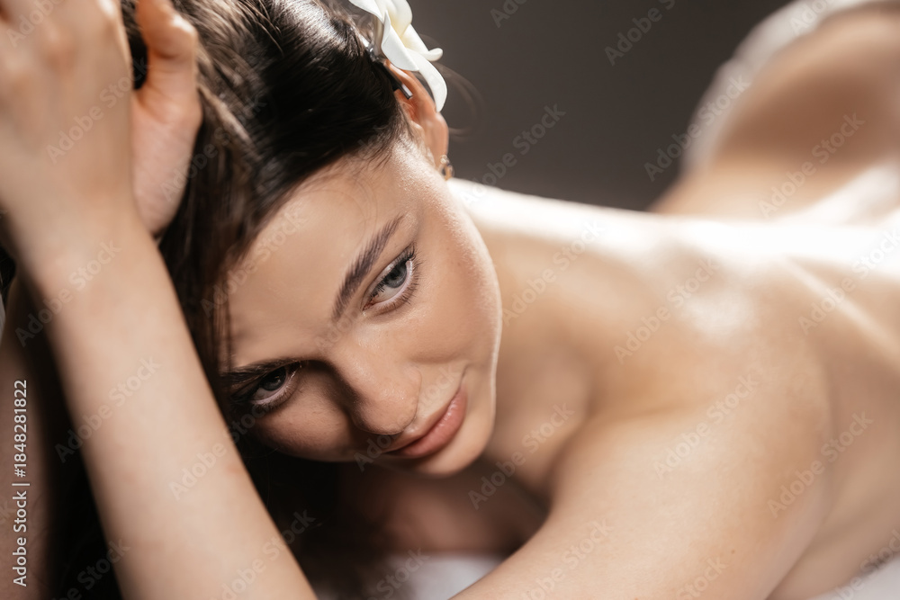 Fototapeta premium Relaxed woman with long dark hair, enjoying a soothing massage in a serene spa environment, surrounded by calming textures and soft lighting, embodying tranquility and wellness