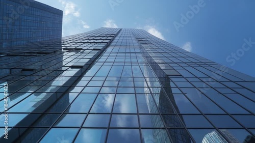 Modern Skyscraper Glass Facade Reflecting Blue Sky and Clouds, Low Angle View of Contemporary Office Building Exterior.