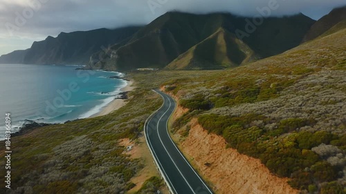 An awe-inspiring aerial view of a winding road cutting through mountains or a coastal landsc.