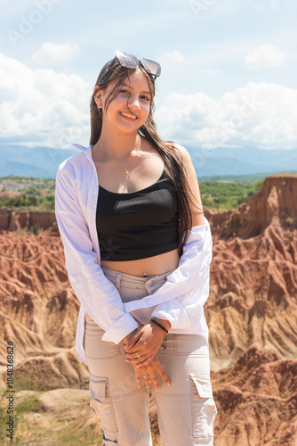 Portrait of a smiling Hispanic teenage girl looking at the camera against the backdrop of the Tatacoa Desert at midday in Villavieja, Huila, Colombia. Concept of tourism and vacations