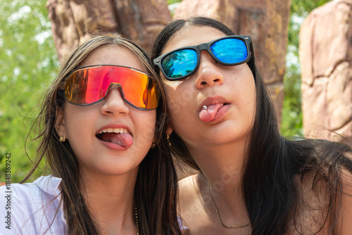 Two cheerful young Latina women wearing glasses and piercings hug while looking at the camera in a park in Villavieja, Huila, Colombia. Concept of femininity and modernity