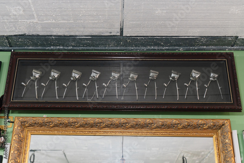 A framed display of vintage manual hair clippers arranged in a row above a decorative mirror in a classic barbershop setting.