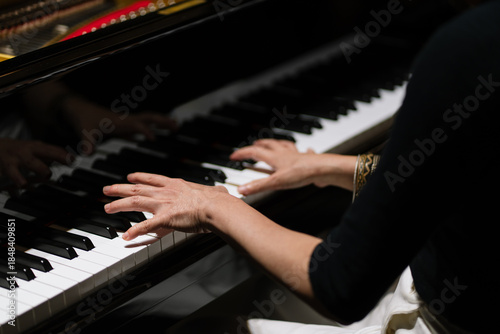 Close-up of a person playing piano with both hands on the keys, captured under dramatic lighting.