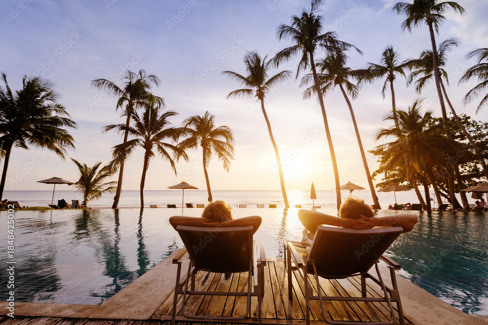 Fototapeta premium honeymoon couple on vacation in luxury beach hotel, man and woman relaxing near swimming pool at sunset