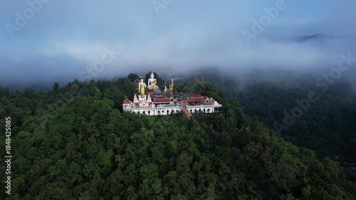 Aerial view of Wat Phra That Doi Kham temple on mountain top surrounded by morning sea of mist and lush green forest in Chiang Mai, Thailand.
