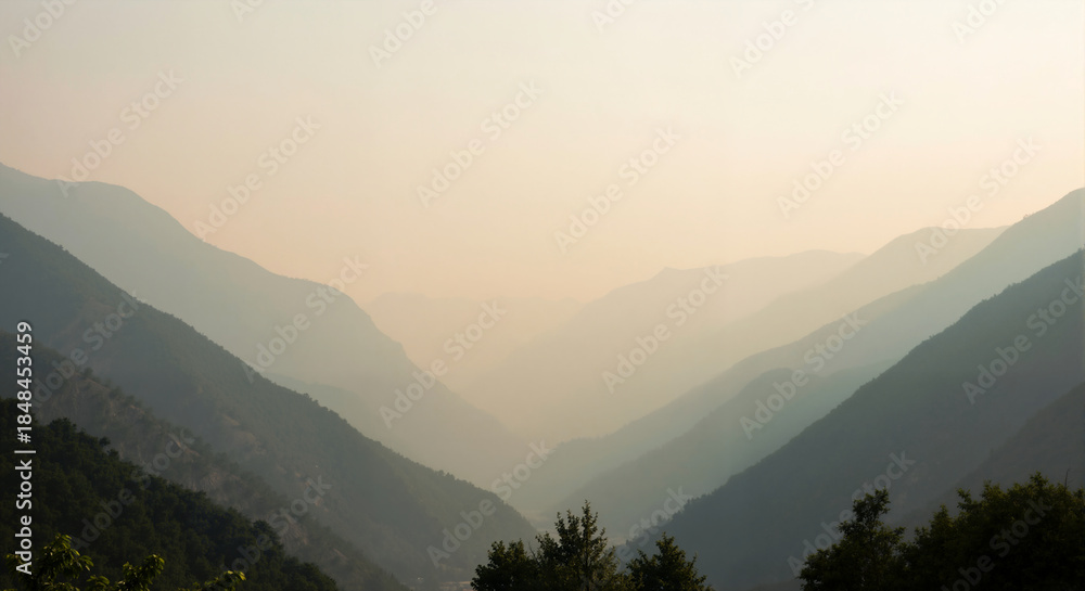 Obraz premium Hazy mountain range landscape with layered silhouettes at sunrise. Scenic view of a valley with atmospheric perspective. Natural background with copy space for text.