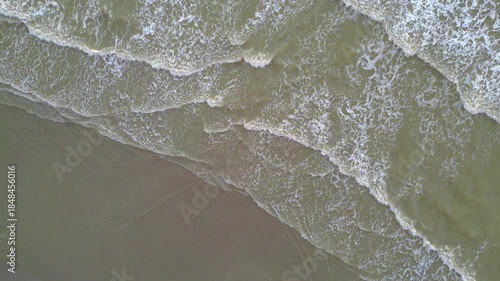 top down aerial view shoreline showing pale green surf, fine sand, repeating foam bands, slow motion rhythm, minimalist texture,