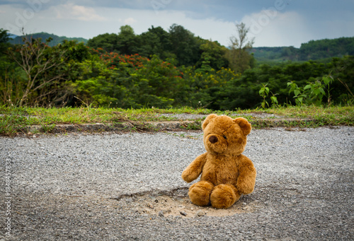 Lonely teddy bear sitting alone on the cracked asphalt road.