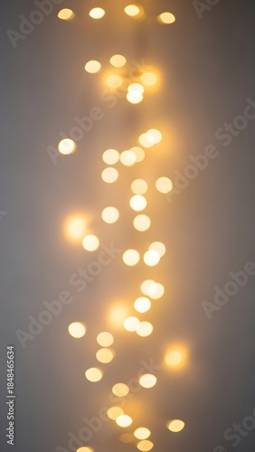 A vertical string of warm, glowing bokeh lights creating a soft, dreamy, and ethereal background against a muted grey surface.