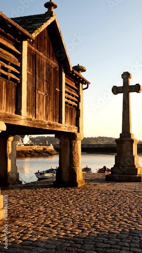 A rustic stilted granary on a stone quay with boats at golden hour