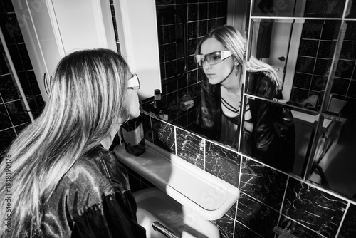 Drunken woman touching her face, looking at her reflection in a bathroom mirror
